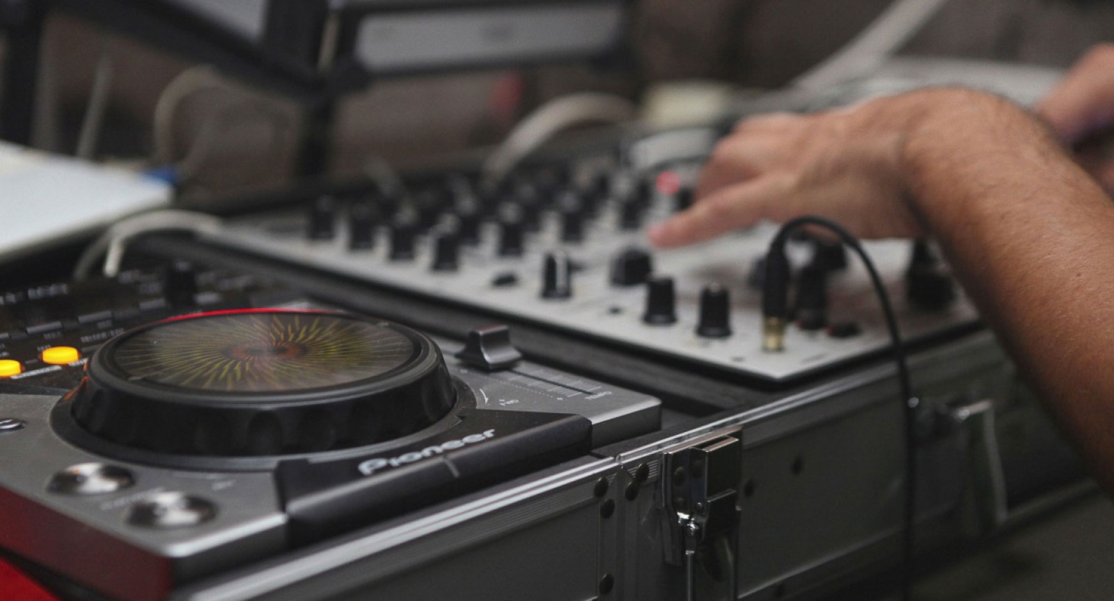 Un DJ impegnato a mixare musica su un mixer professionale. La mano è sopra i controlli, con attrezzatura musicale visibile.