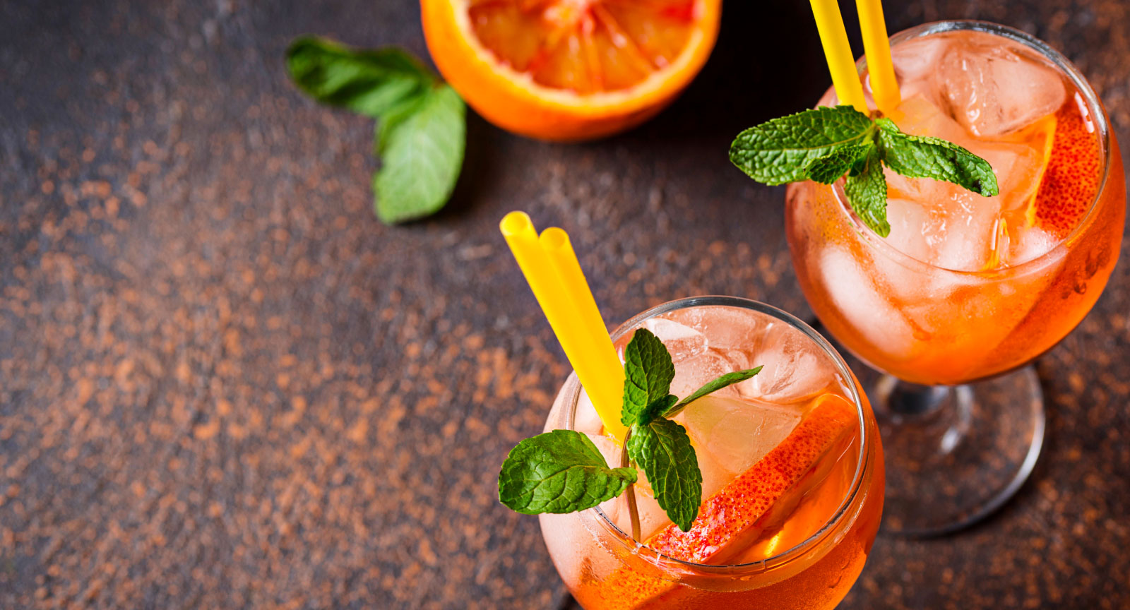 Due cocktail rinfrescanti a base di agrumi, decorati con foglie di menta e cannucce gialle, su uno sfondo rustico.