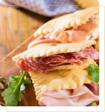 Tre triangle di pasta ripiena su un tagliere di legno, farciti con vari salumi come prosciutto, salame e mortadella.