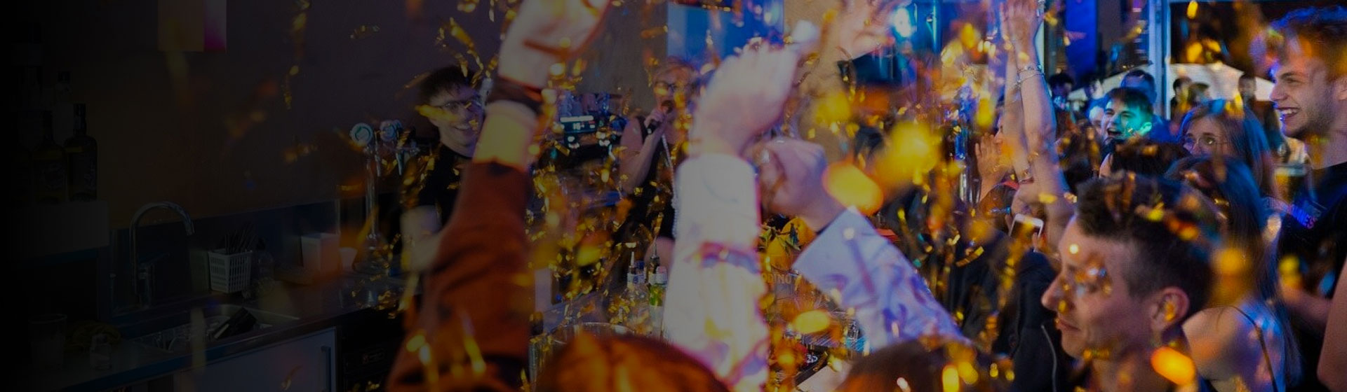 Un gruppo di persone si diverte a una festa, con le mani alzate mentre cade della confetti dorati, creando un'atmosfera festosa e vivace.