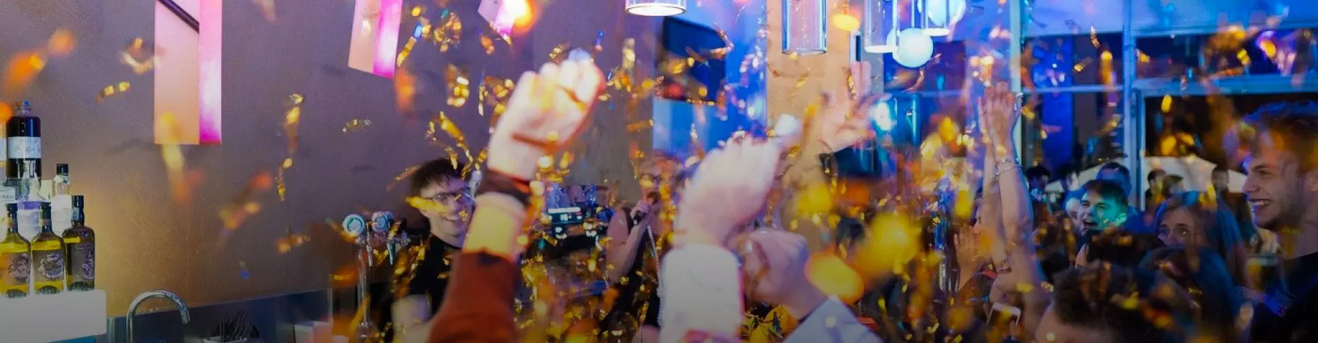 Eventi e feste private. Una vivace festa in un locale notturno con persone che ballano e ridono, circondate da coriandoli dorati che volano nell'aria, creando un'atmosfera di gioia e celebrazione.