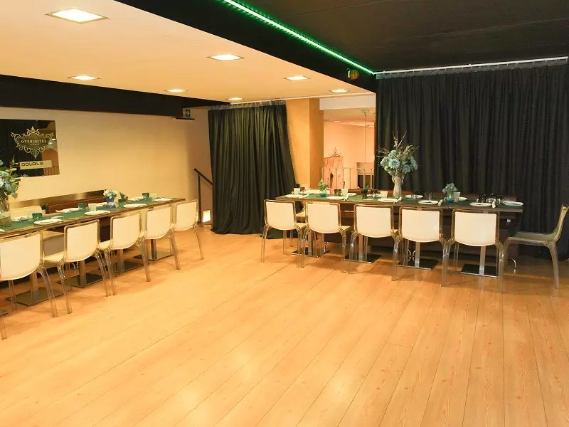 Interno di un ristorante elegante con un lungo tavolo apparecchiato, sedie bianche e decorazioni floreali blu, ambientazione curata e luminosa.