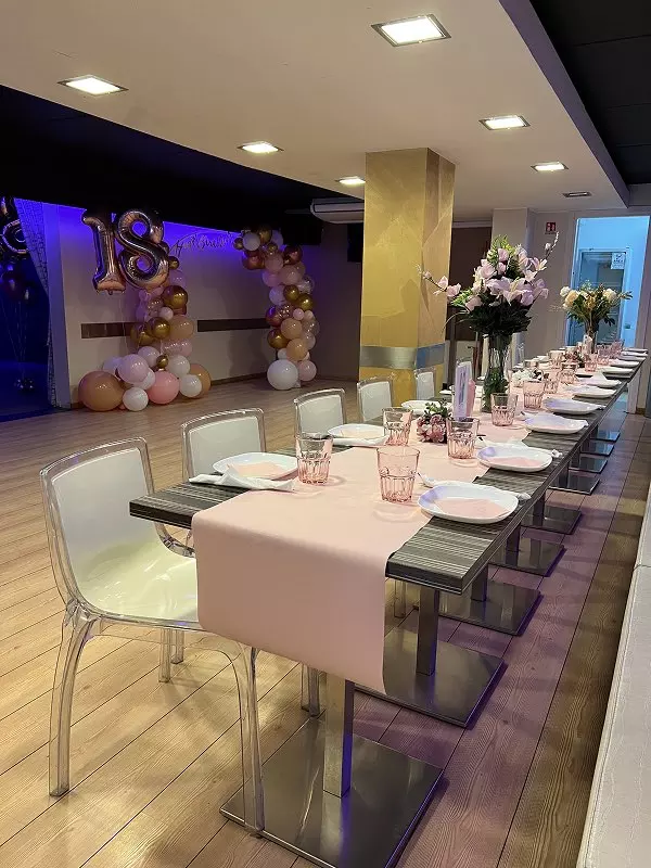 Immagine di un tavolo elegantemente apparecchiato per una festa di compleanno, con decorazioni rosa e oro, palloncini e un'atmosfera festiva.