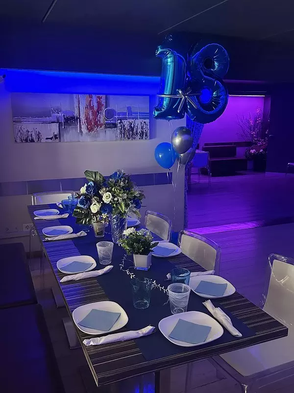 Un elegante tavolo decorato con fiori blu e bianchi, piatti e bicchieri pronti per una festa di compleanno con palloncini blu e un numero 10.
