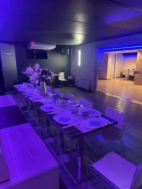 Un elegante ristorante moderno con un tavolo ben apparecchiato, decorato con fiori, posate lucide e illuminazione blu, creando un'atmosfera accogliente e sofisticata.
