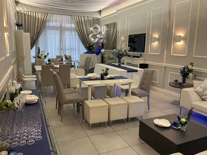 Una elegante sala festiva decorata per un evento speciale, con tavoli imbanditi e fiori blu e bianchi. Arredamento moderno.