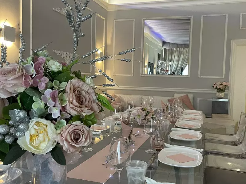 Tavola elegante apparecchiata per un evento, decorata con un bouquet di fiori rosa e dettagli scintillanti, in un ambiente raffinato.