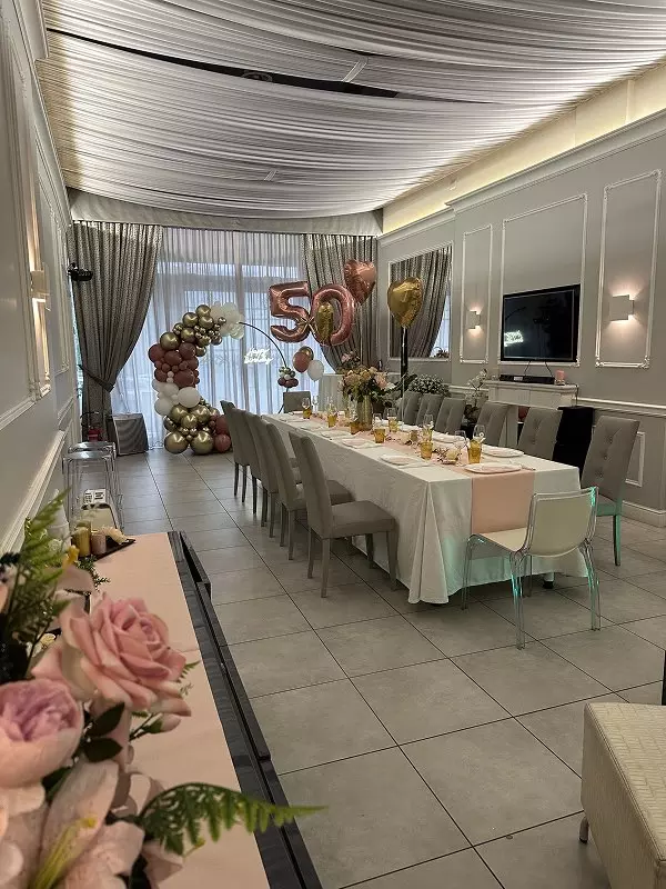 Un elegante tavolo apparecchiato per una festa con decorazioni rosa, oro e palloncini, festeggiando un cinquantesimo compleanno.