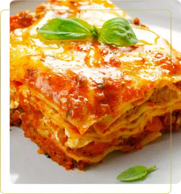 Pranzo. Porzione di lasagna dorata e filante, con strati di pasta, carne e salsa di pomodoro, decorata con foglie di basilico fresco.