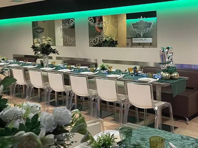 Sala Gialla. Immagine di una sala da pranzo elegantemente allestita per un evento, con un lungo tavolo decorato, sedie trasparenti e centrotavola floreali.