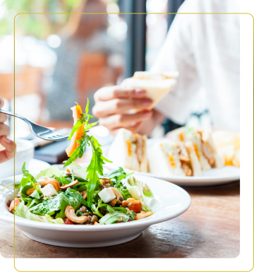 Un primo piano di un piatto di insalata fresca con verdure e noci, mentre una persona tiene un sandwich in un ristorante.
