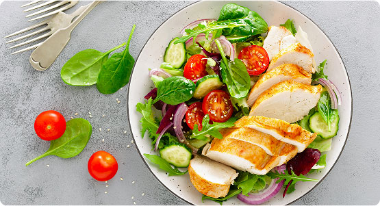 Insalata fresca con pollo grigliato, pomodorini, cetrioli e cipolla rossa su un piatto bianco, con decorazioni di spinaci. Un piatto sano e colorato.