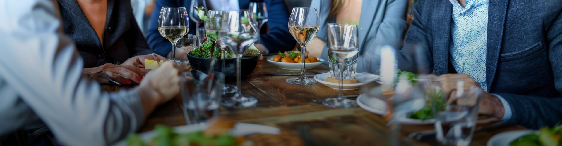 Un tavolo elegante con calici di vino bianco, cibo gourmet e persone che si godono una cena raffinata. Dettagli di piatti e bicchieri abbelliscono l'atmosfera conviviale.